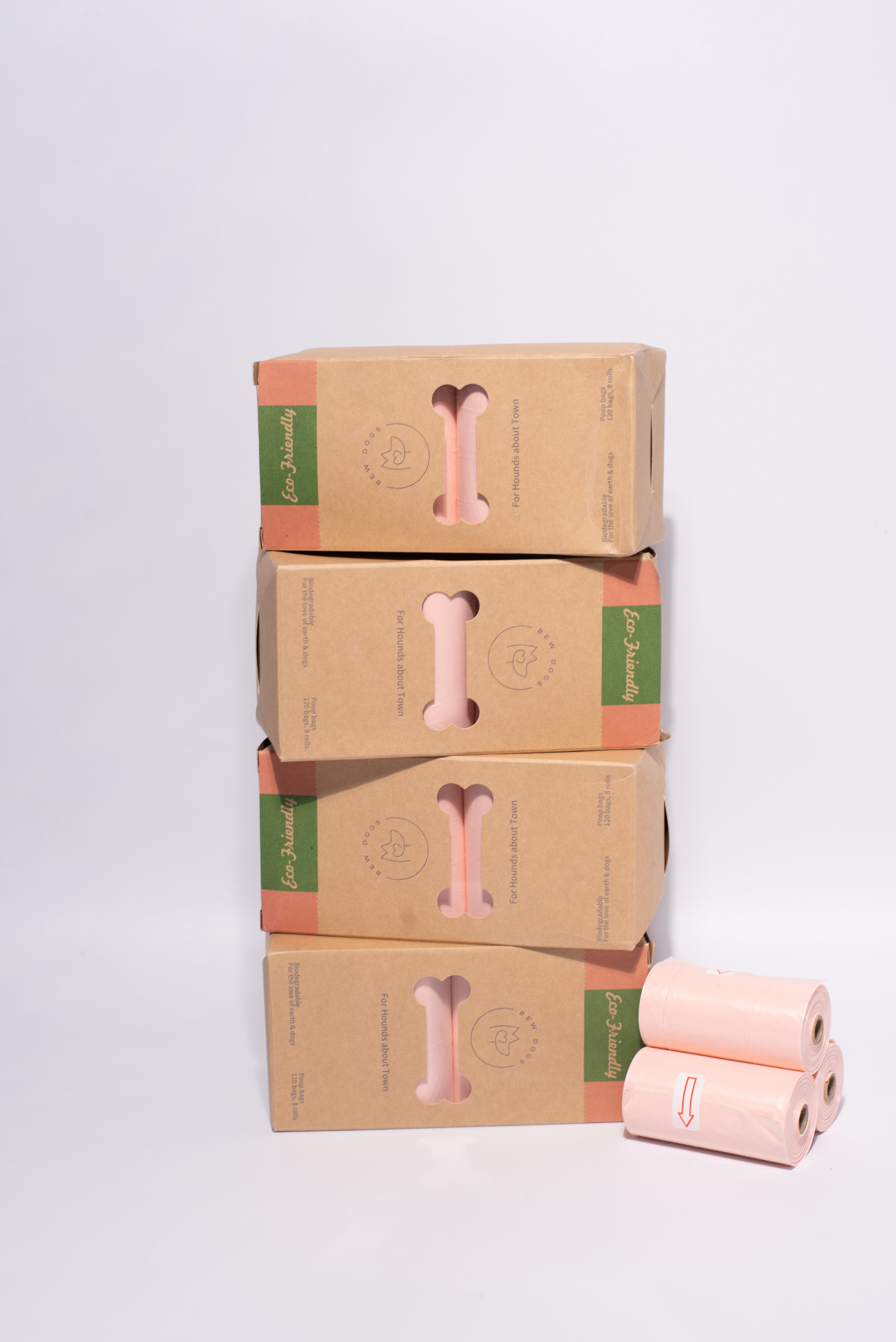 4 boxes of bew dogs strong, eco-friendly and biodegradable poo bags stacked on top of each other, with 3 rolls of peach bags in front, sitting in front of a grey background