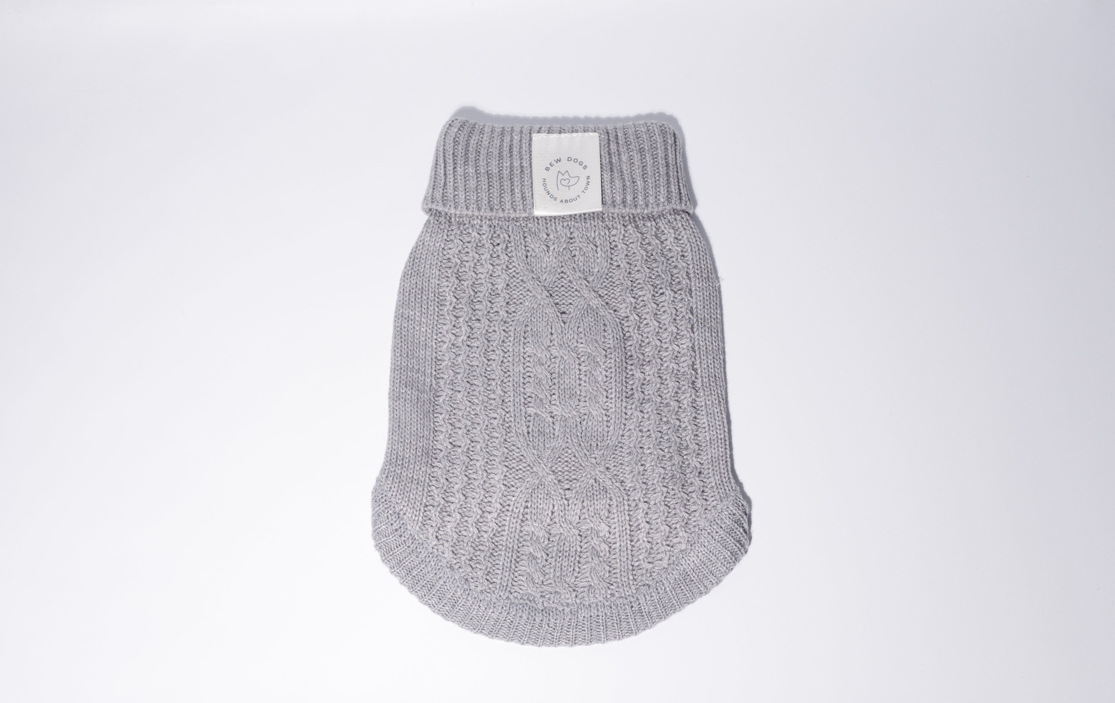 A light gray knit dog jumper with a cable-knit pattern and a white Bew Dogs brand label on the collar, shown against a plain light gray background - perfect for puppies and small dogs 