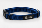 A blue velvet dog collar with a black plastic buckle, black metal ring, and a black brand patch that reads 'BEW DOGS' with a logo, shown on a light grey studio background - this collar is fully adjustable, available in 3 sizes and super soft 