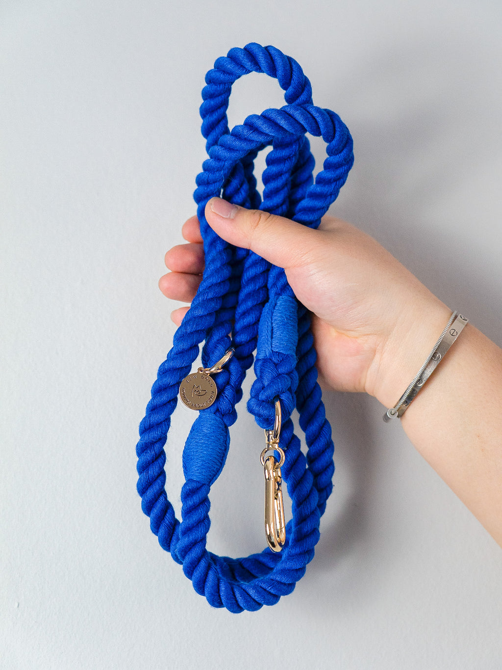 Hand holding a deep royal blue rope dog leash with a gold clasp on a light grey background, the photo shows this is a soft but strong lead suitable for all dogs