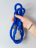 Hand holding a deep royal blue rope dog leash with a gold clasp on a light grey background, the photo shows this is a soft but strong lead suitable for all dogs