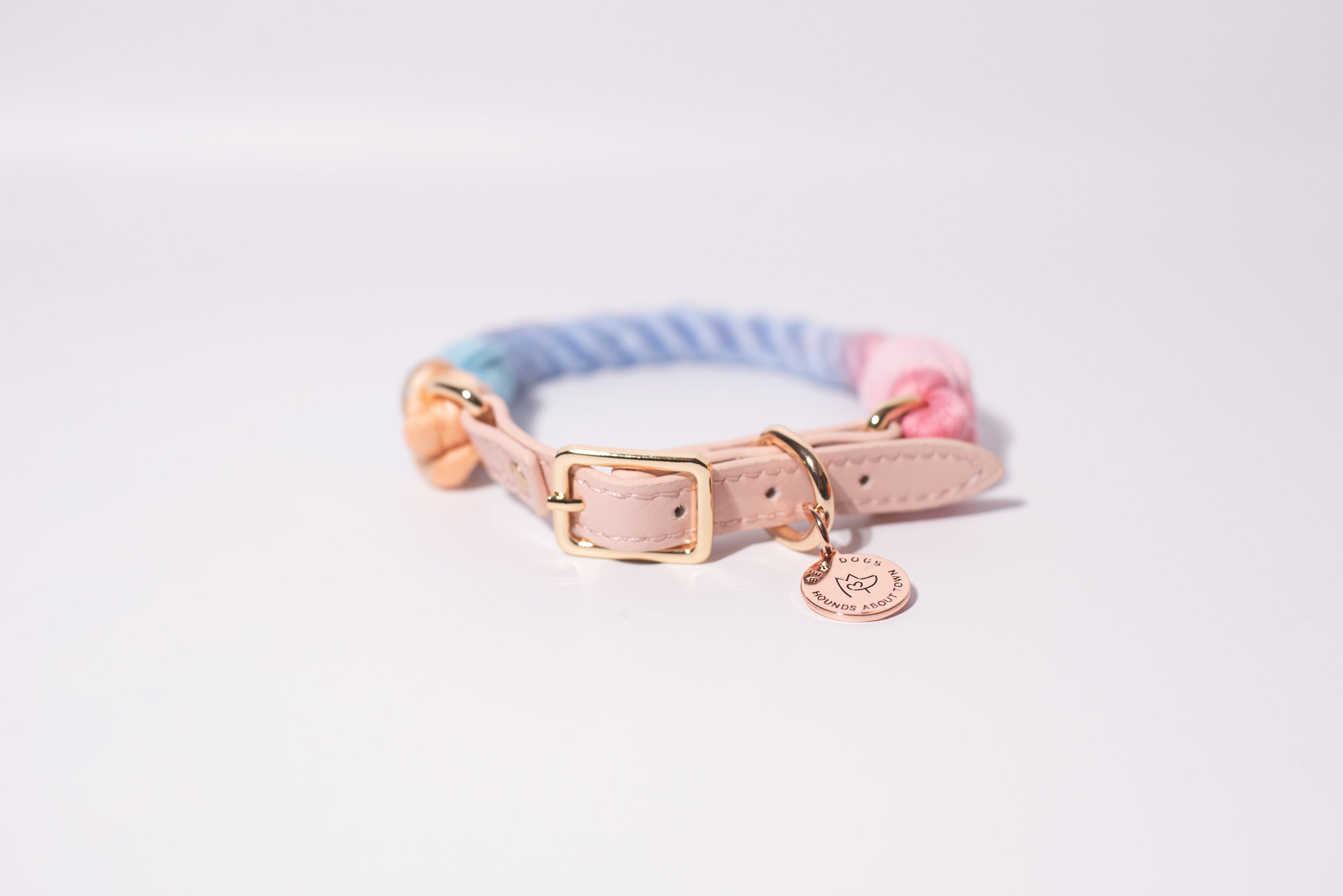 a studio shot set against a white background, of a rainbow rope collar with a gold buckle and bew dogs tag