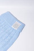 A close-up of a light blue cable-knit fabric dog jumper, featuring a white rectangular brand label that reads 'Bew DOGs’ - perfect for puppies and small dogs 