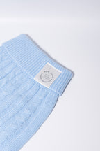 A close-up of a light blue cable-knit fabric dog jumper, featuring a white rectangular brand label that reads 'Bew DOGs’ - perfect for puppies and small dogs 
