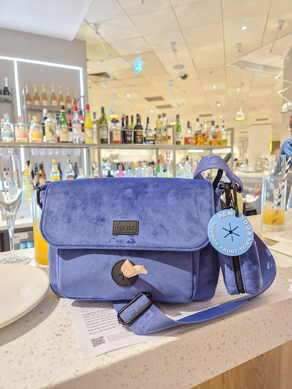 blue velvet dog walking bag, with multiplet compartments for poo bags, pool loop and treats, is sitting on top of a bar