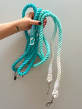 A hand holds an aqua blue and white rope lead for dogs of all shapes and sizes, against a grey wall. This rope lead is durable and stylish.