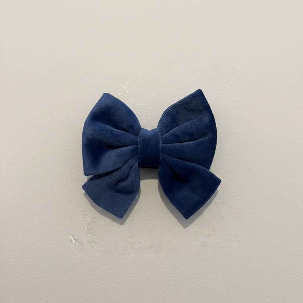 A DEEP BLUE VELVET SAILOR BOW FOR DOGS, SITS AGAINST A PLAIN BACKGROUND.
