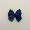 A DEEP BLUE VELVET SAILOR BOW FOR DOGS, SITS AGAINST A PLAIN BACKGROUND.