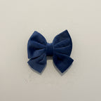 A DEEP BLUE VELVET SAILOR BOW FOR DOGS, SITS AGAINST A PLAIN BACKGROUND.