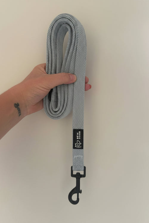 A soft and stylish blue herringbone dog lead, suitable for everyday walks, is held in front of a white background