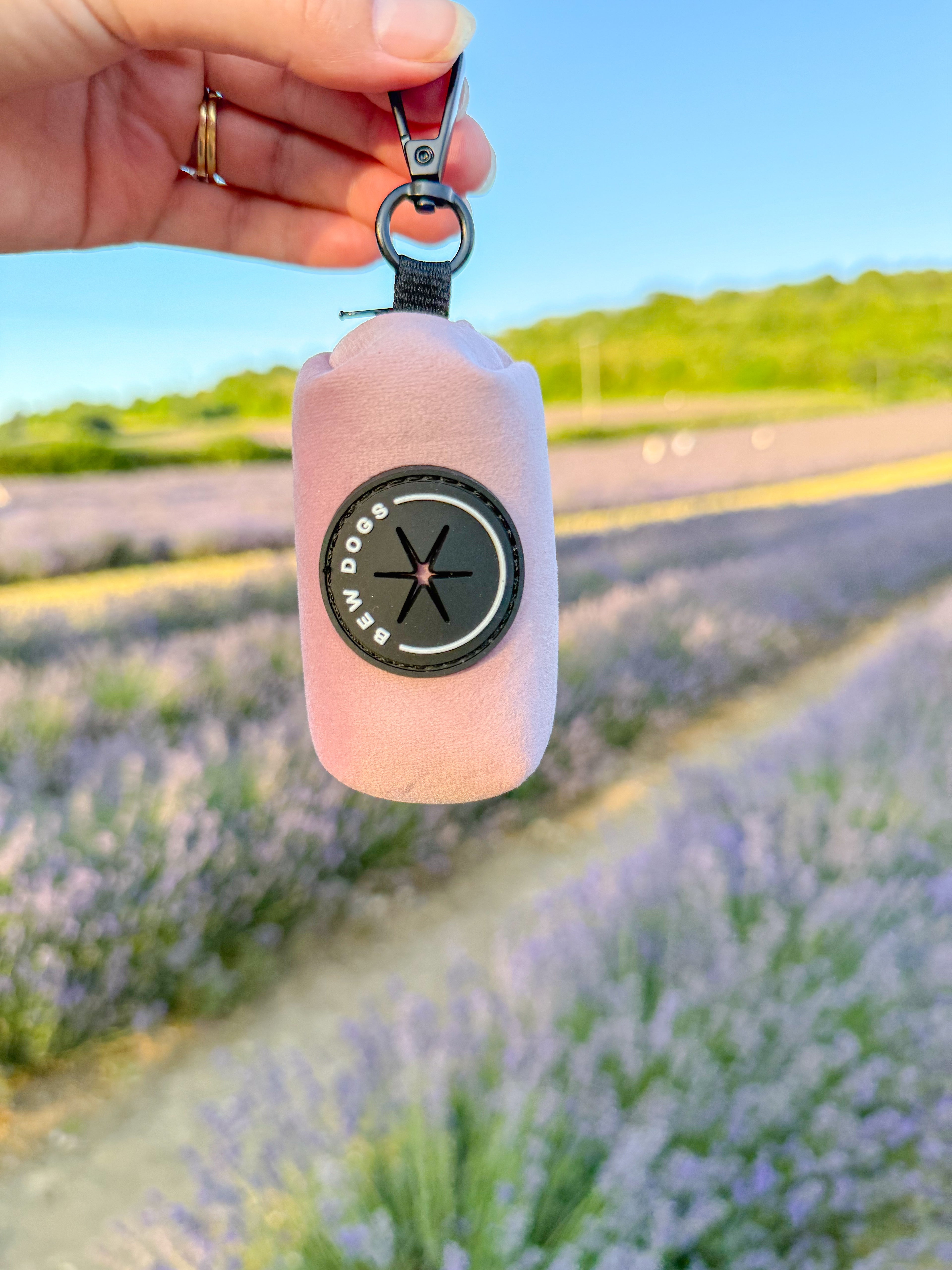 a pink velvet poo bag holder, perfect dog accessory, is held in front of a blurred background of lavender fields