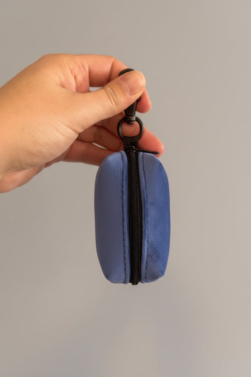 a deep blue velvet holder shown with the zip forward, for storing clean poo bags, is held by a hand in front of a grey wall