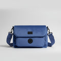 A stunning midnight blue velvet dog walking bag, with specialist compartments for all dog walking essentials, and black details, is shown against a grey background in a studio. 