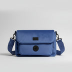A stunning midnight blue velvet dog walking bag, with specialist compartments for all dog walking essentials, and black details, is shown against a grey background in a studio. 