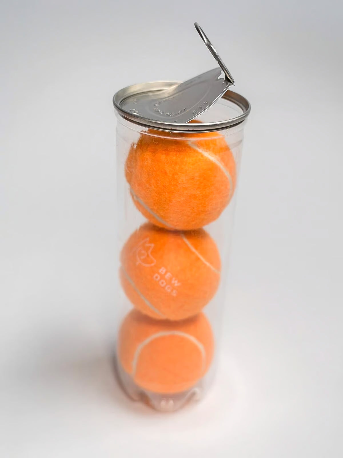 Three orange tennis balls in a clear plastic container with a metal lid on a white background. perfect toys for dogs of all sizes.
