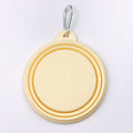 A pastel yellow collapsible dog bowl with a silver metal carabiner clip, shown folded on a clean white background.