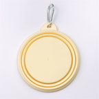 A pastel yellow collapsible dog bowl with a silver metal carabiner clip, shown folded on a clean white background.