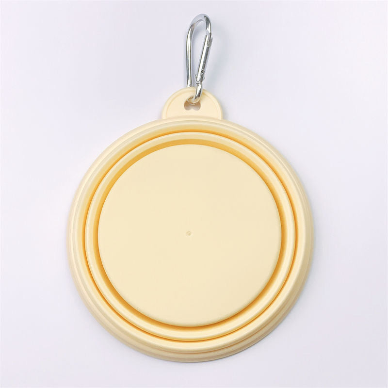 A pastel yellow collapsible dog bowl with a silver metal carabiner clip, shown folded on a clean white background.