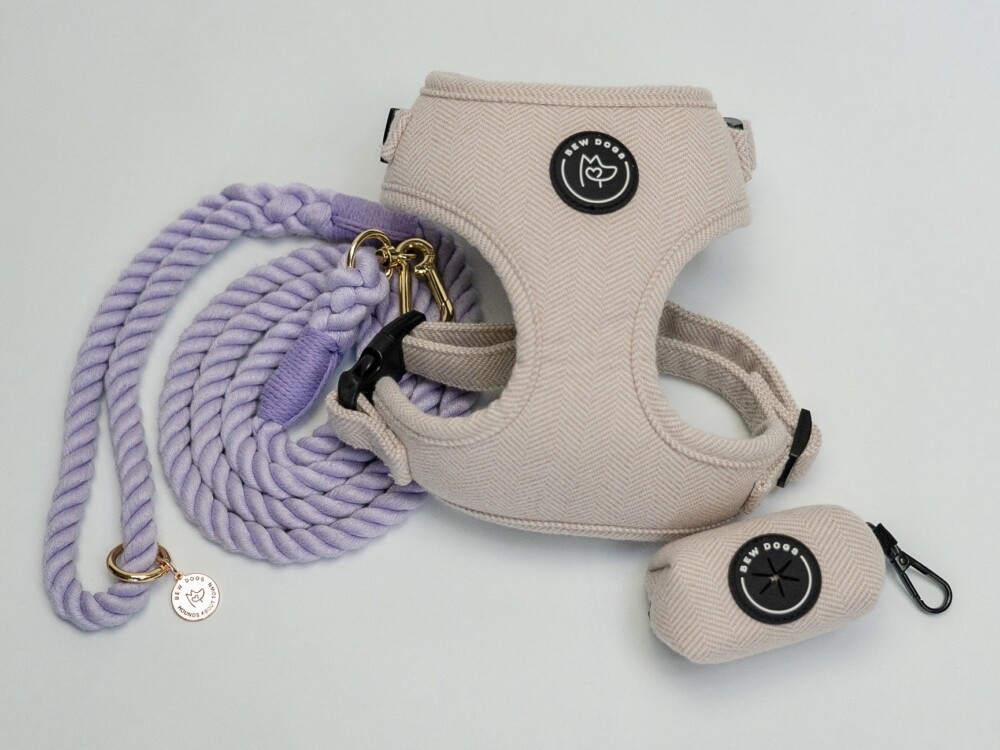 a bundle of stylish dog accessories, including a harness, poo bag holder and rope lead in lilac, against a white background.
