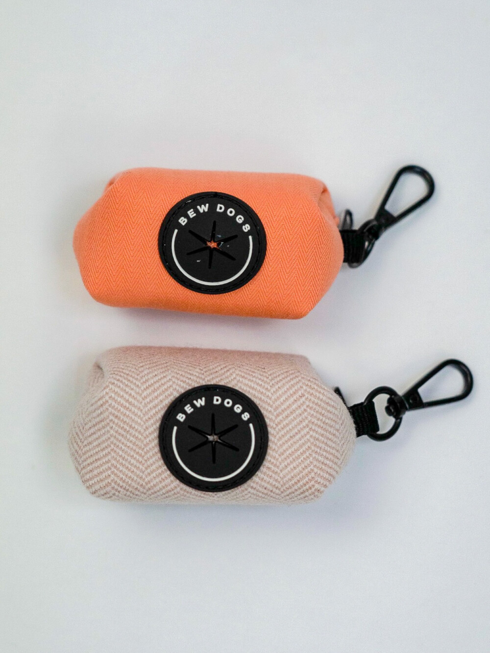 two dog poo bag holders, against a white background, in bright peach and lilac herringbone patterns