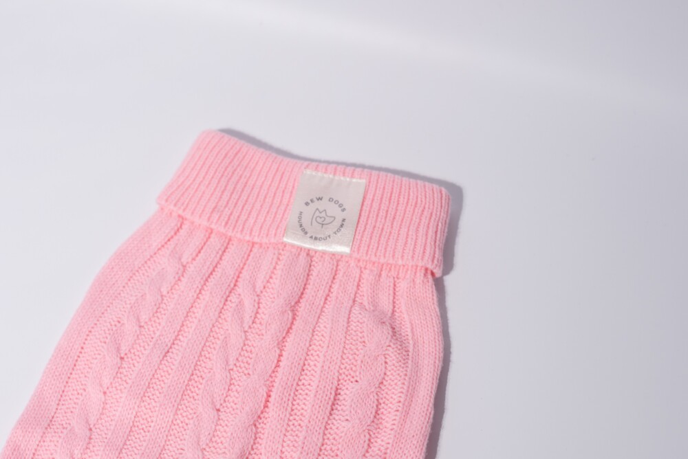 A close up of a pink cable knit jumper against a white background