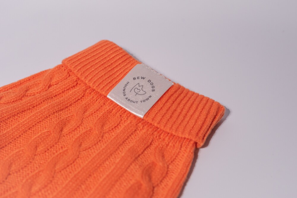 A close up of an orange cable knit jumper on a white background