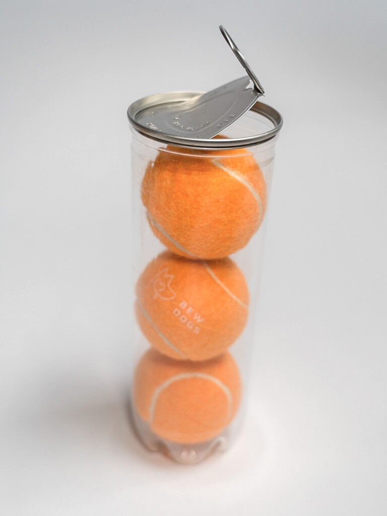A plastic tube containing three orange tennis balls, with an opened ring pull