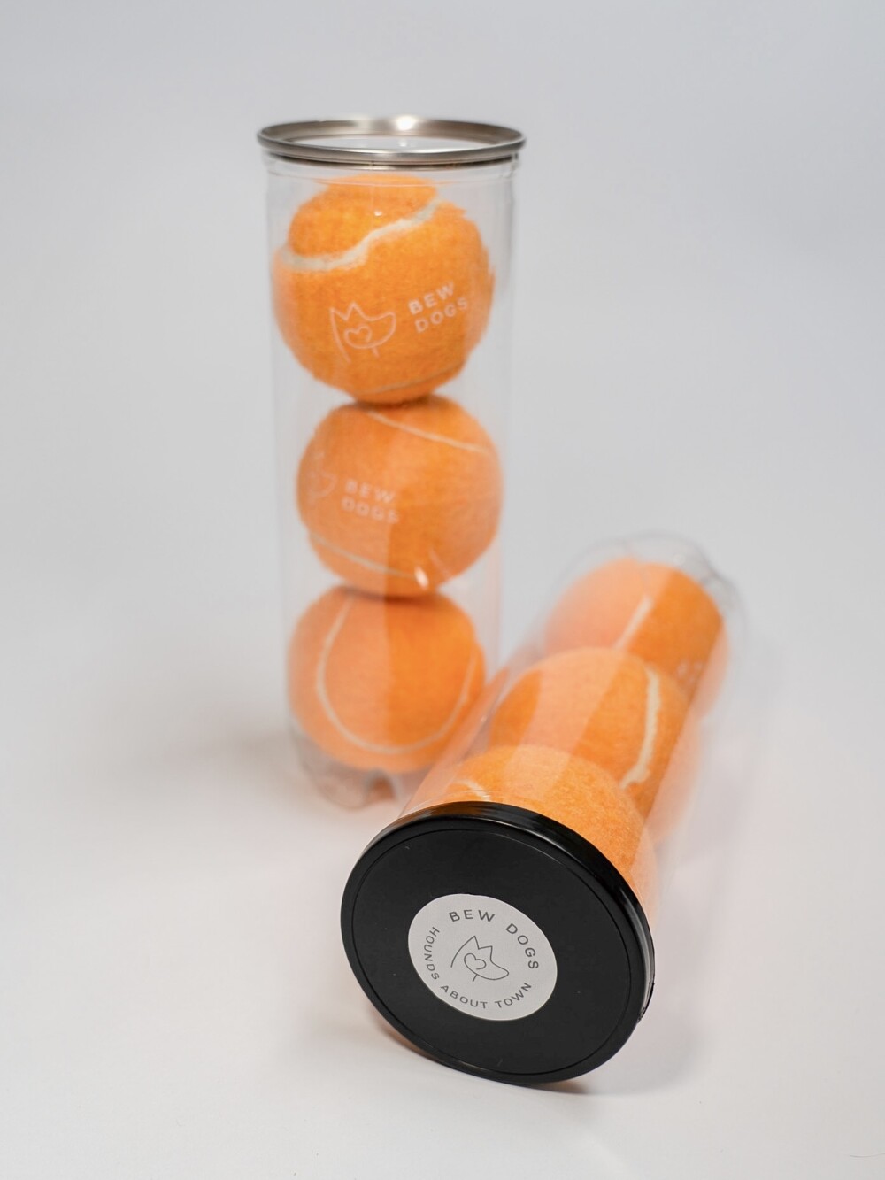 Two tubes, each containing three orange tennis balls for dogs