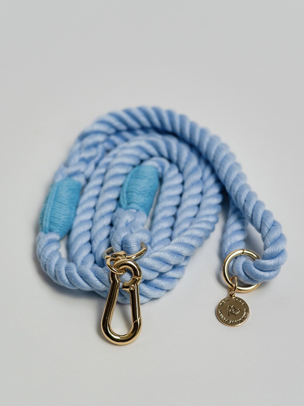 A sky blue rope lead with gold clasp and logo, against a white background