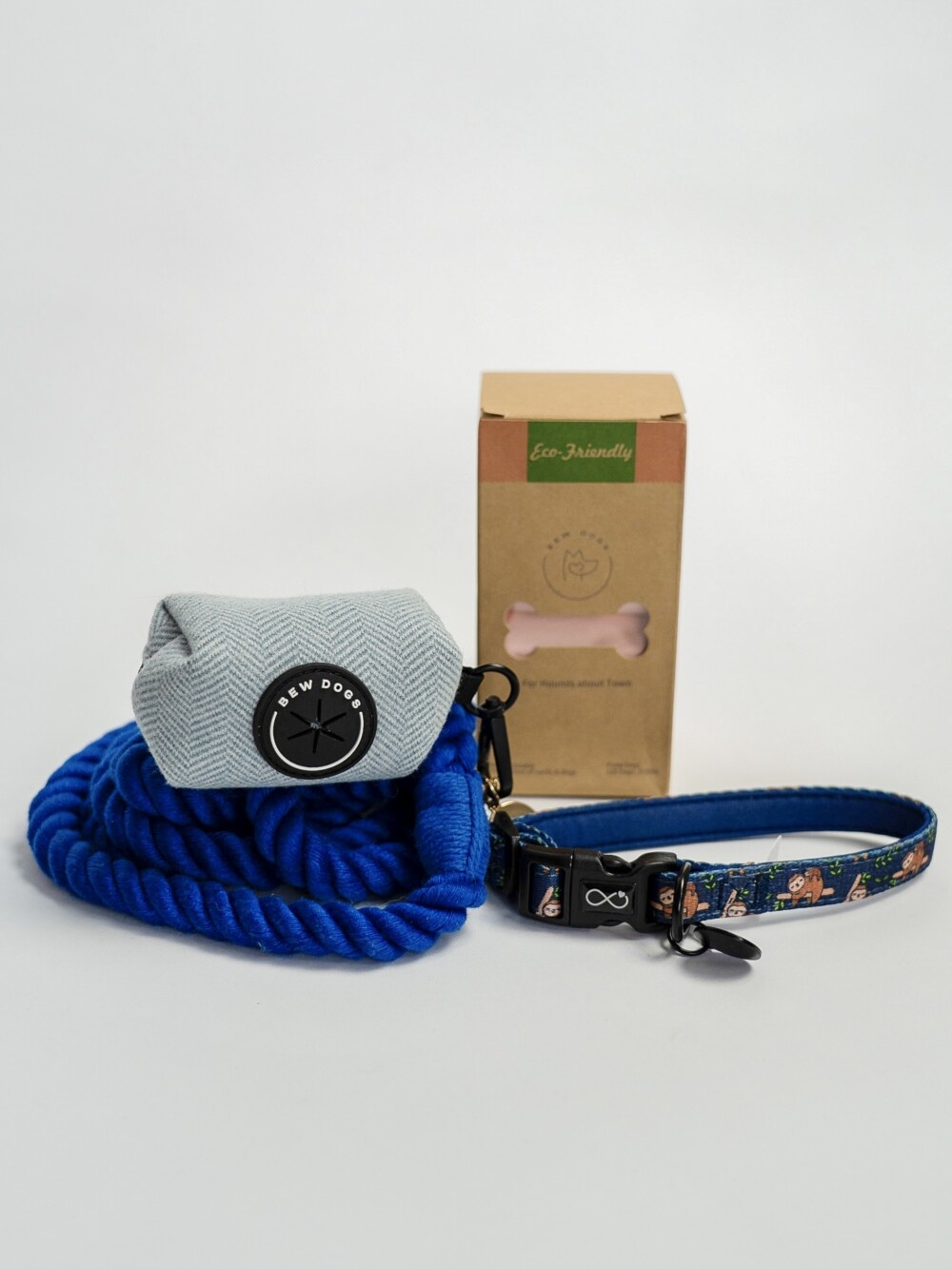 A bundle of products, including a deep blue rope lead, blue herringbone poop bag holder, a box of eco friendly poo bags and a blue collar, against a white background