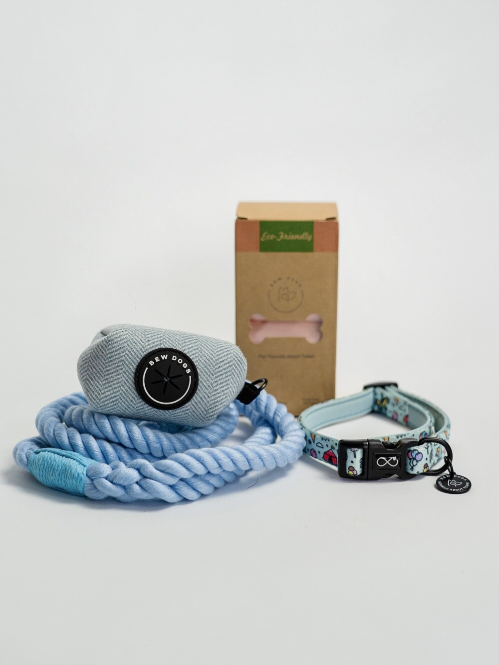 A bundle of products, including a sky blue rope lead, blue herringbone poop bag holder, a box of eco friendly poo bags and a sky blue collar, against a white background