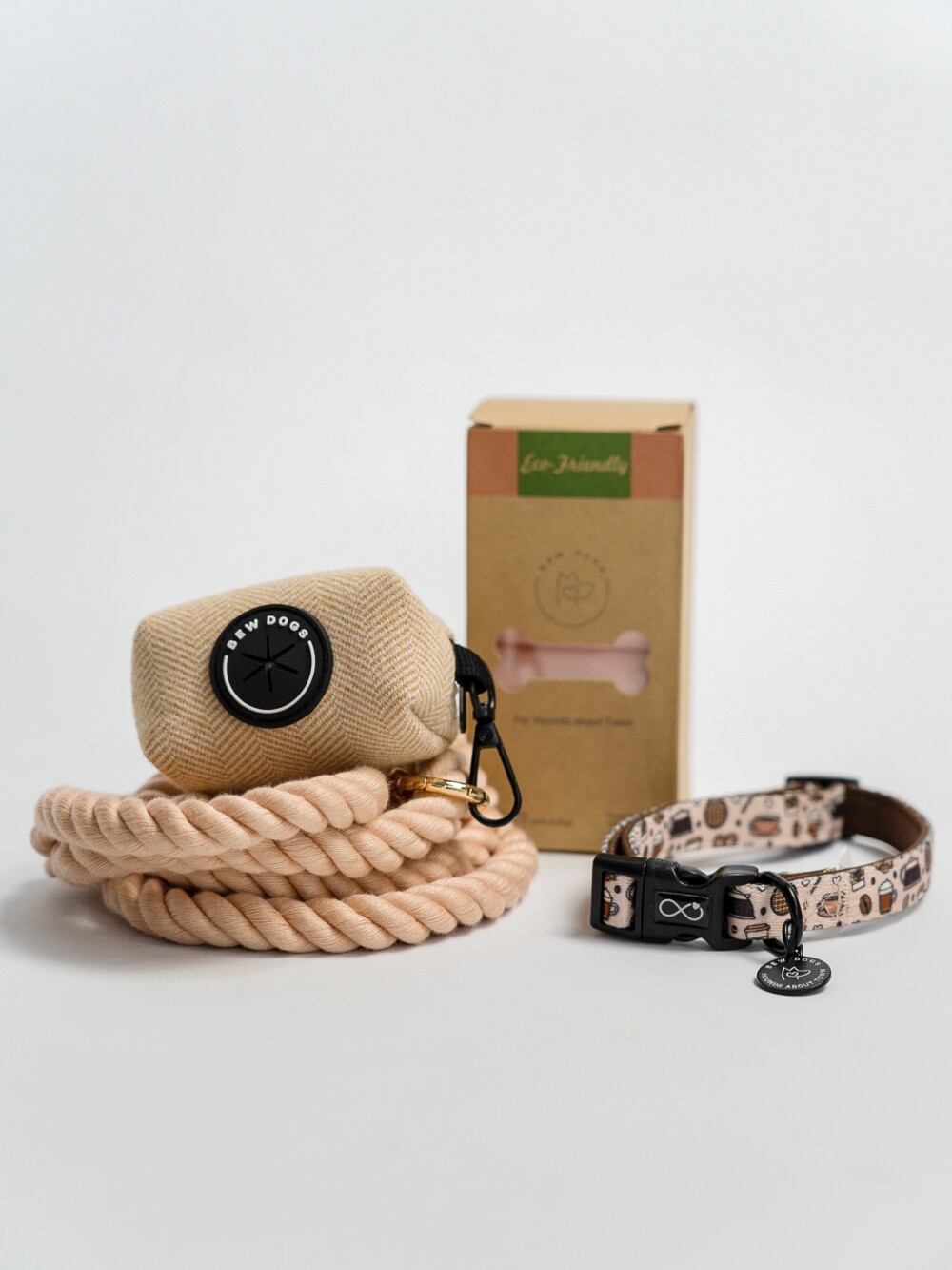 A cream rope lead, herringbone poop bag holder, a box of eco-friendly poop bags and a cream collar, against a white background.