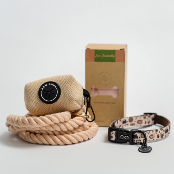 A cream rope lead, herringbone poop bag holder, a box of eco-friendly poop bags and a cream collar, against a white background.