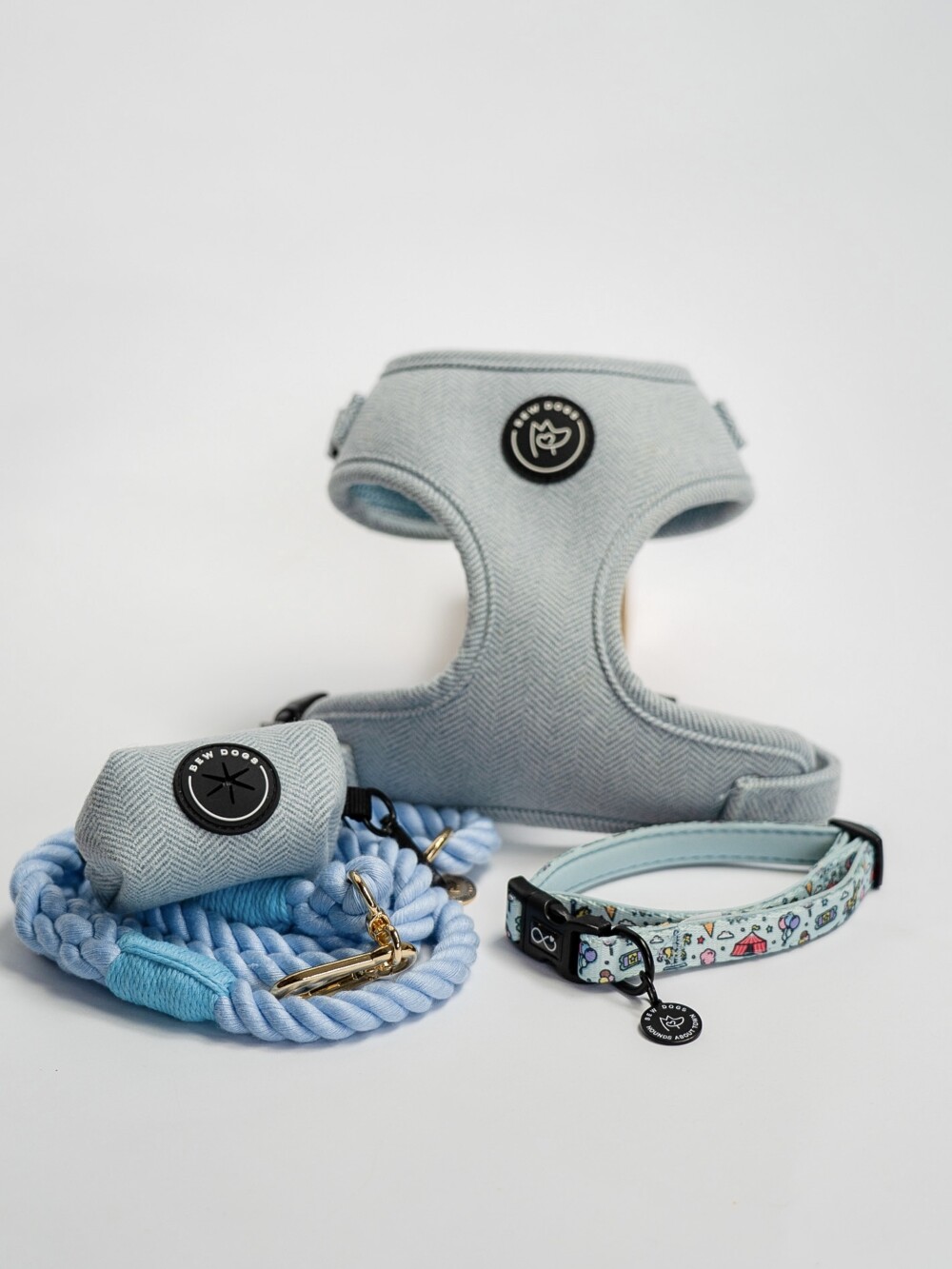 A sky blue herringbone harness, matching poop bag holder and rope lead plus a blue/green collar, against a white background.