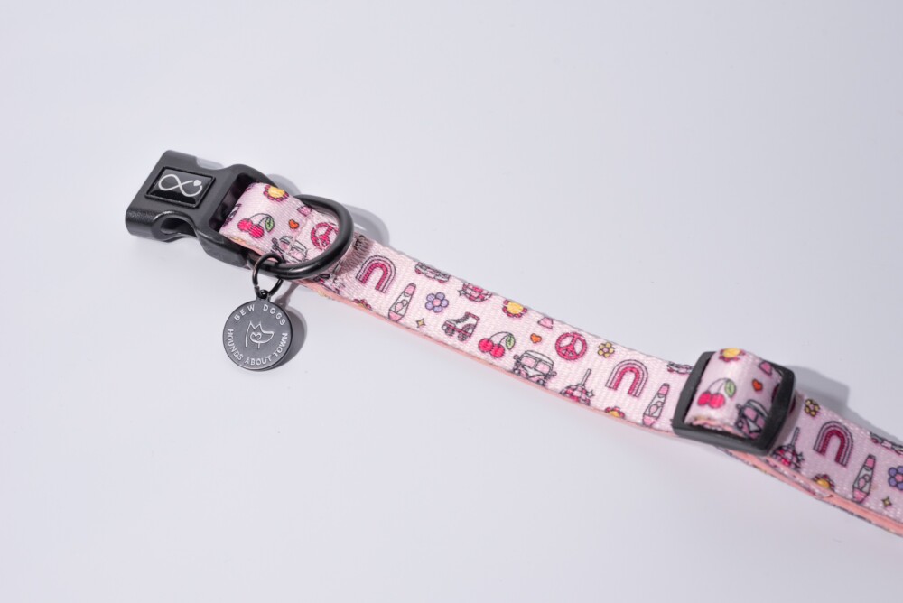 A close up of a pink neoprene collar against a white background, with a bew dogs tag.