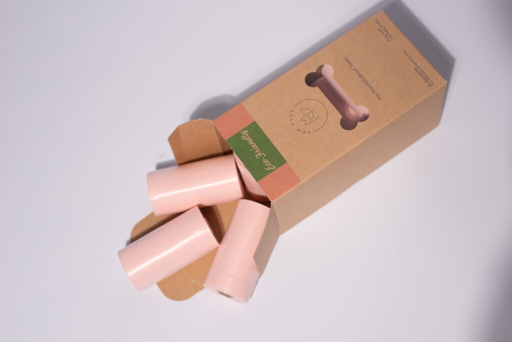 An opened box of Eco-friendly Poop bags with a few rolls falling out the box, against a white background.