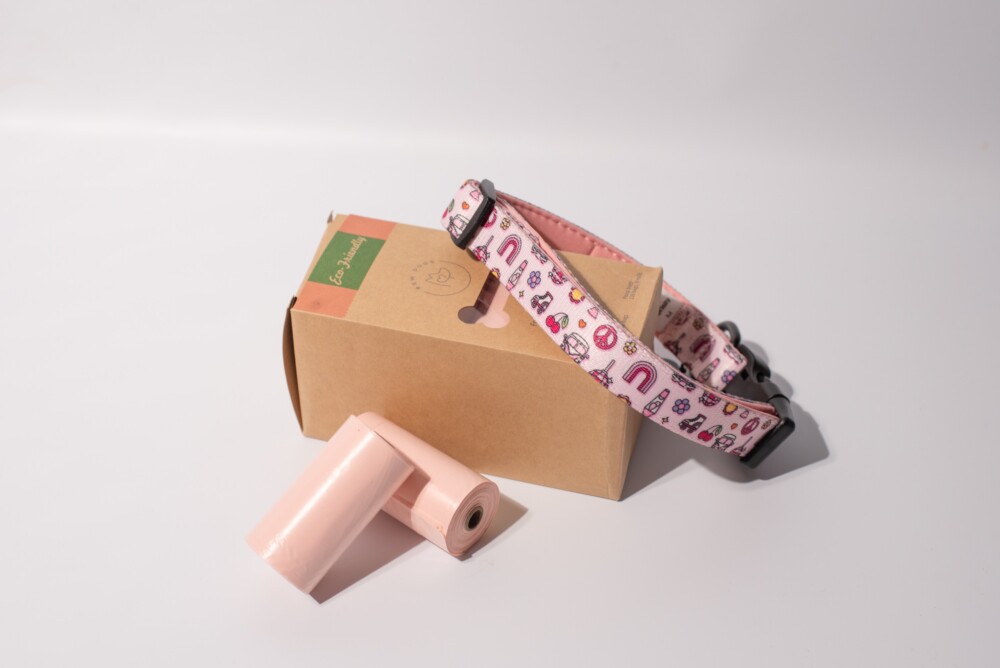 A box of eco-friendly peach poop bags with a pink neoprene collar, against a white background.