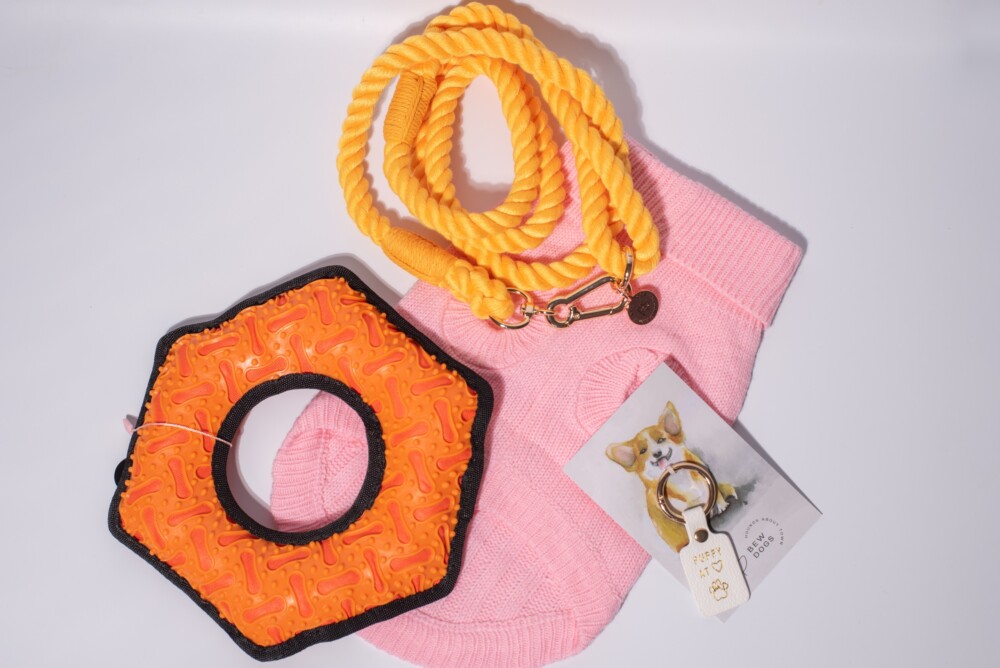 A bundle of dog accessories including a pink cable knit jumper, orange honey rope lead and an orange hex durable toy.