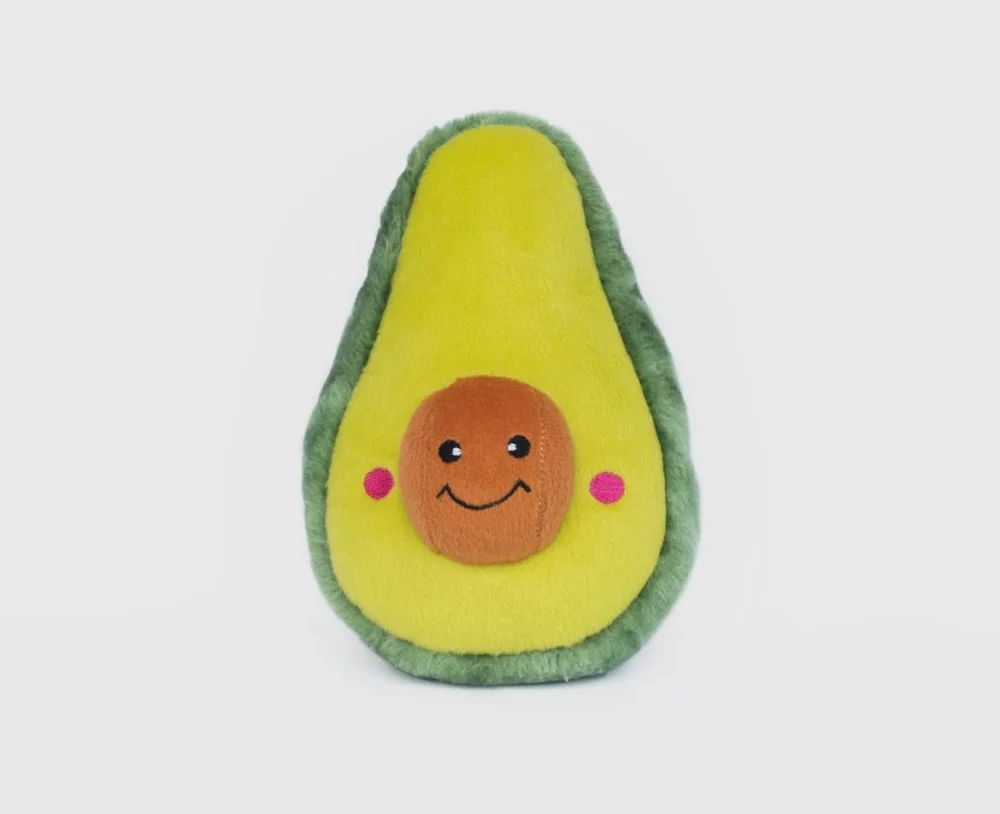 A large plush green avocado dog toy, with a smiley face in the stone, set against a white background