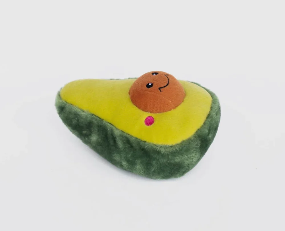 A large plush green avocado dog toy, with a smiley face in the stone, from a side view, set against a white background