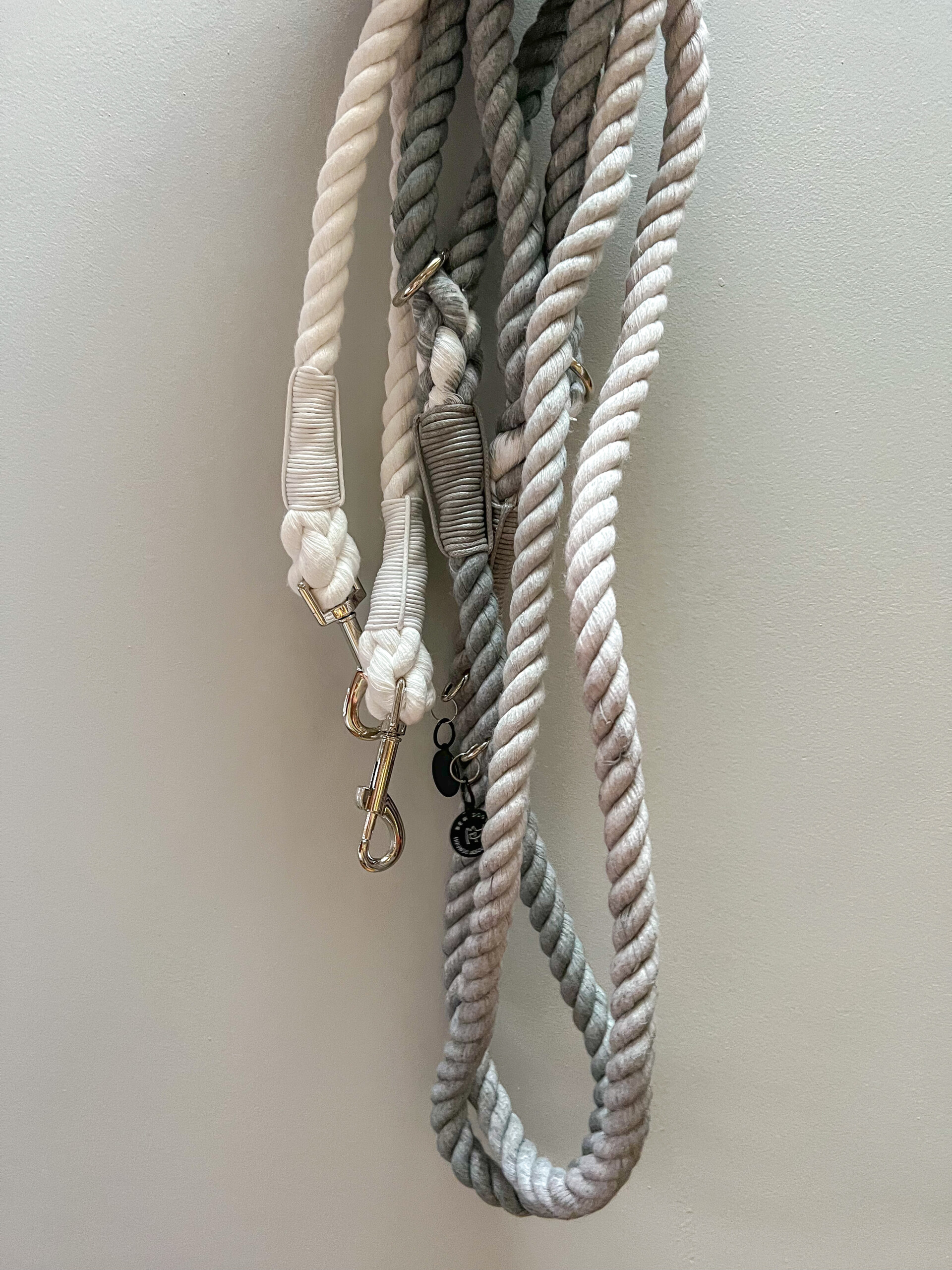 A grey ombre luxury rope lead, being held by a woman with deep and dark red painted nails against a grey painted wall
