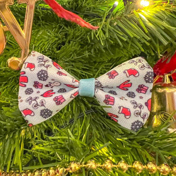 A winter dog bow tie, showing a festive and snow scene, placed on a Christmas tree amongst decorations