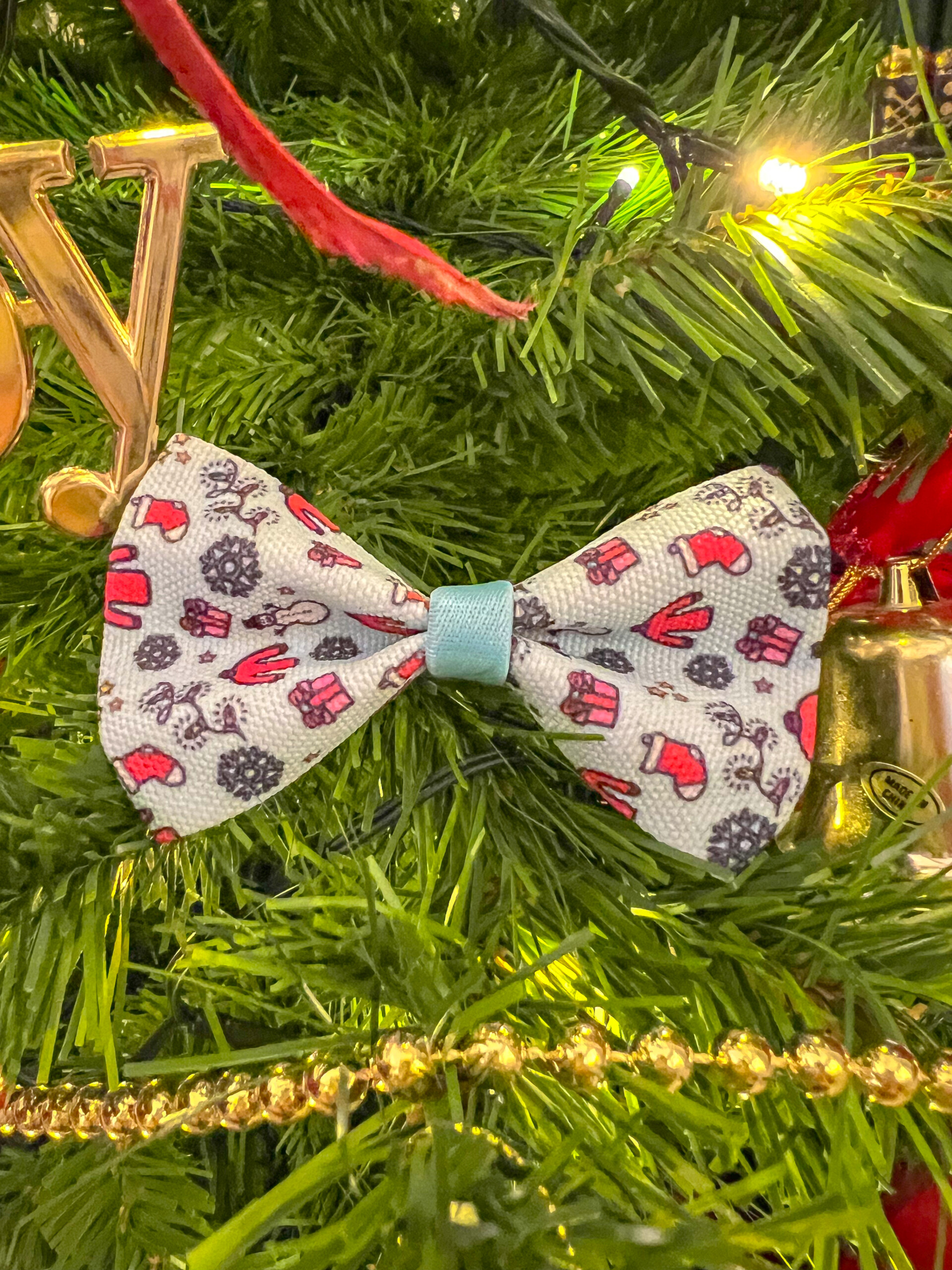 A winter dog bow tie, showing a festive and snow scene, placed on a Christmas tree amongst decorations