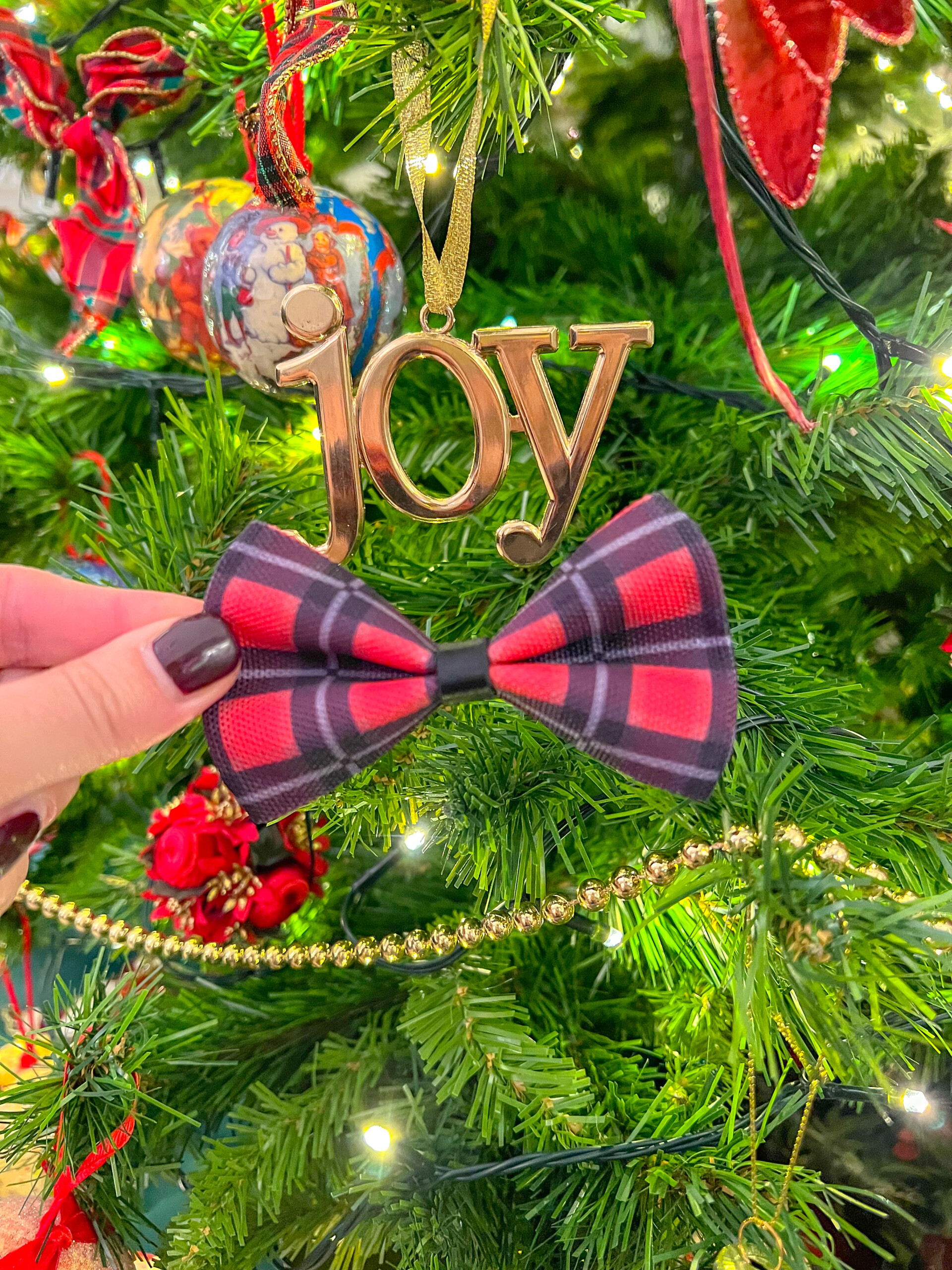 A winter dog bow tie, in a festive red checked pattern, placed on a Christmas tree amongst decorations.