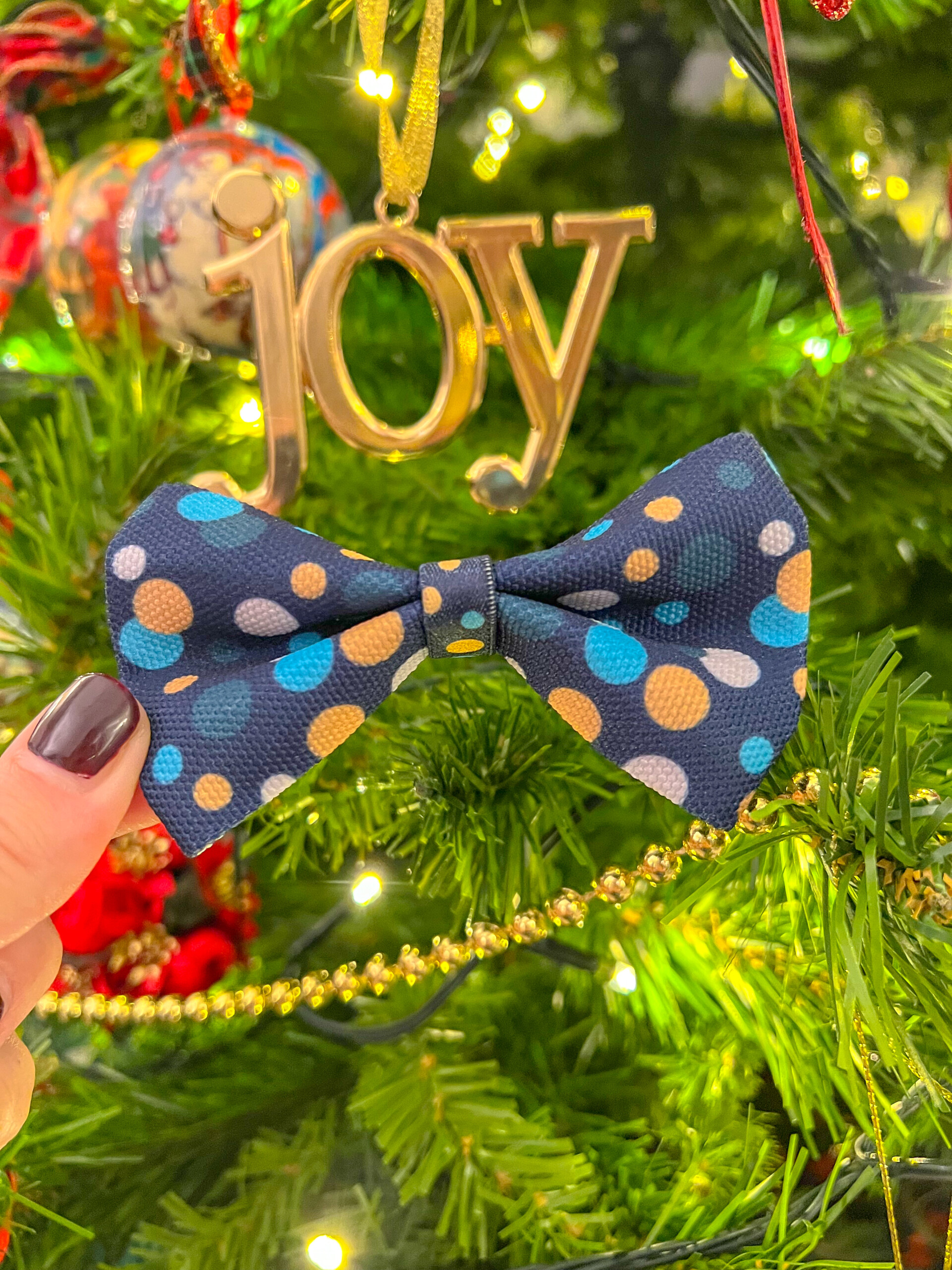 A winter dog bow tie, in a festive pattern with gold and blue spots on a dark blue background.