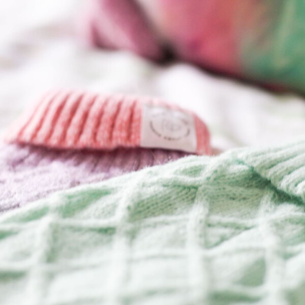a close up of a green and rainbow coloured cable knit jumpers for cats and dogs, laid flat - the background is unfocused