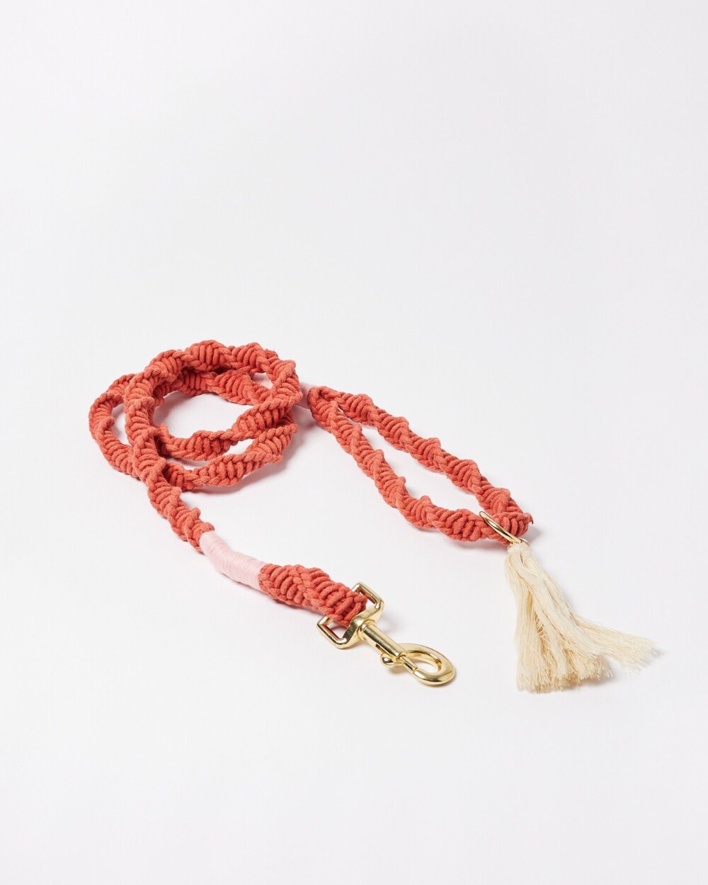 a pinkish, sunset coloured twister rope lead with a tassel and gold detail glasp, shown against a white background