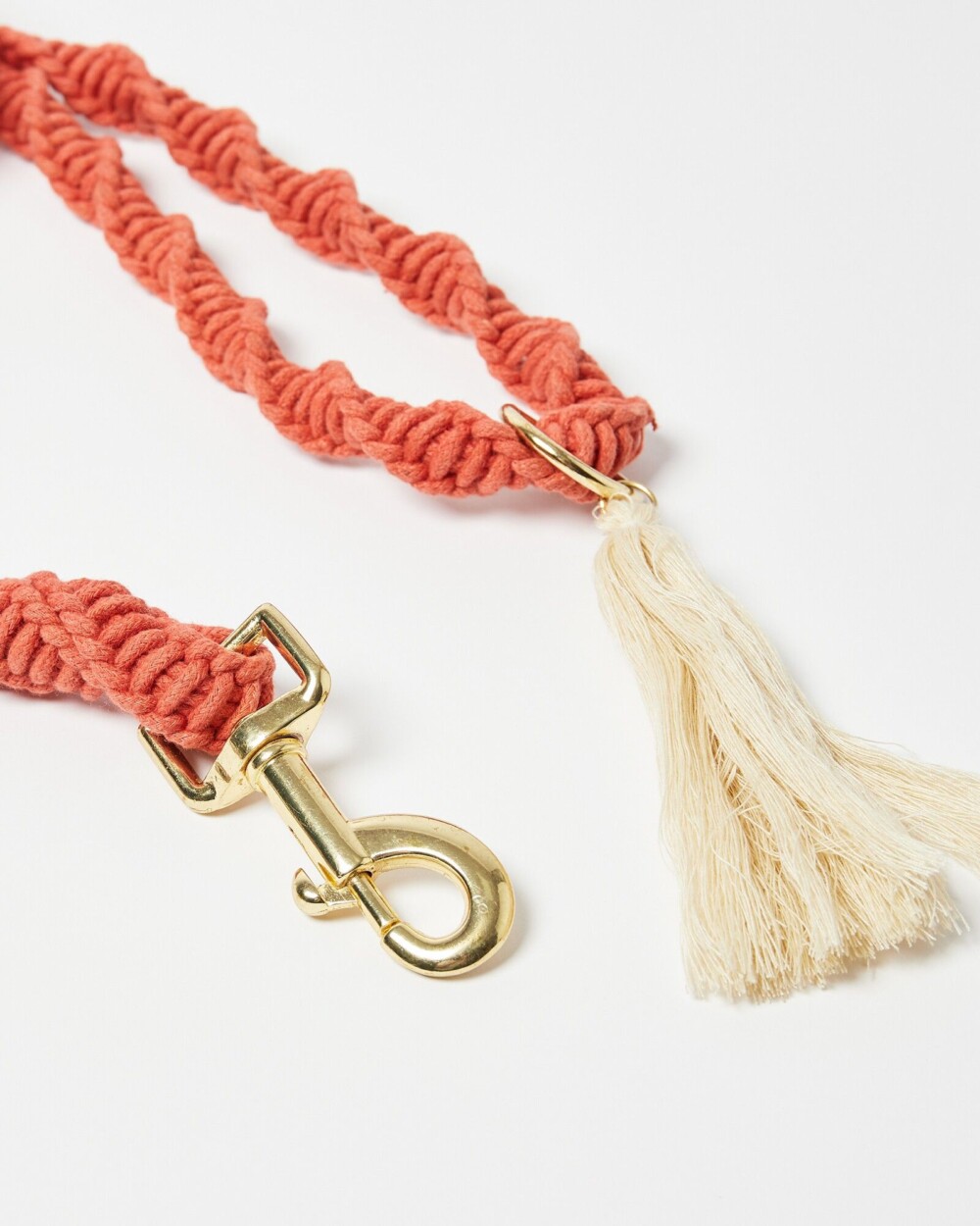 a pinkish, sunset coloured twister rope lead with a tassel and gold detail glasp, shown against a white background