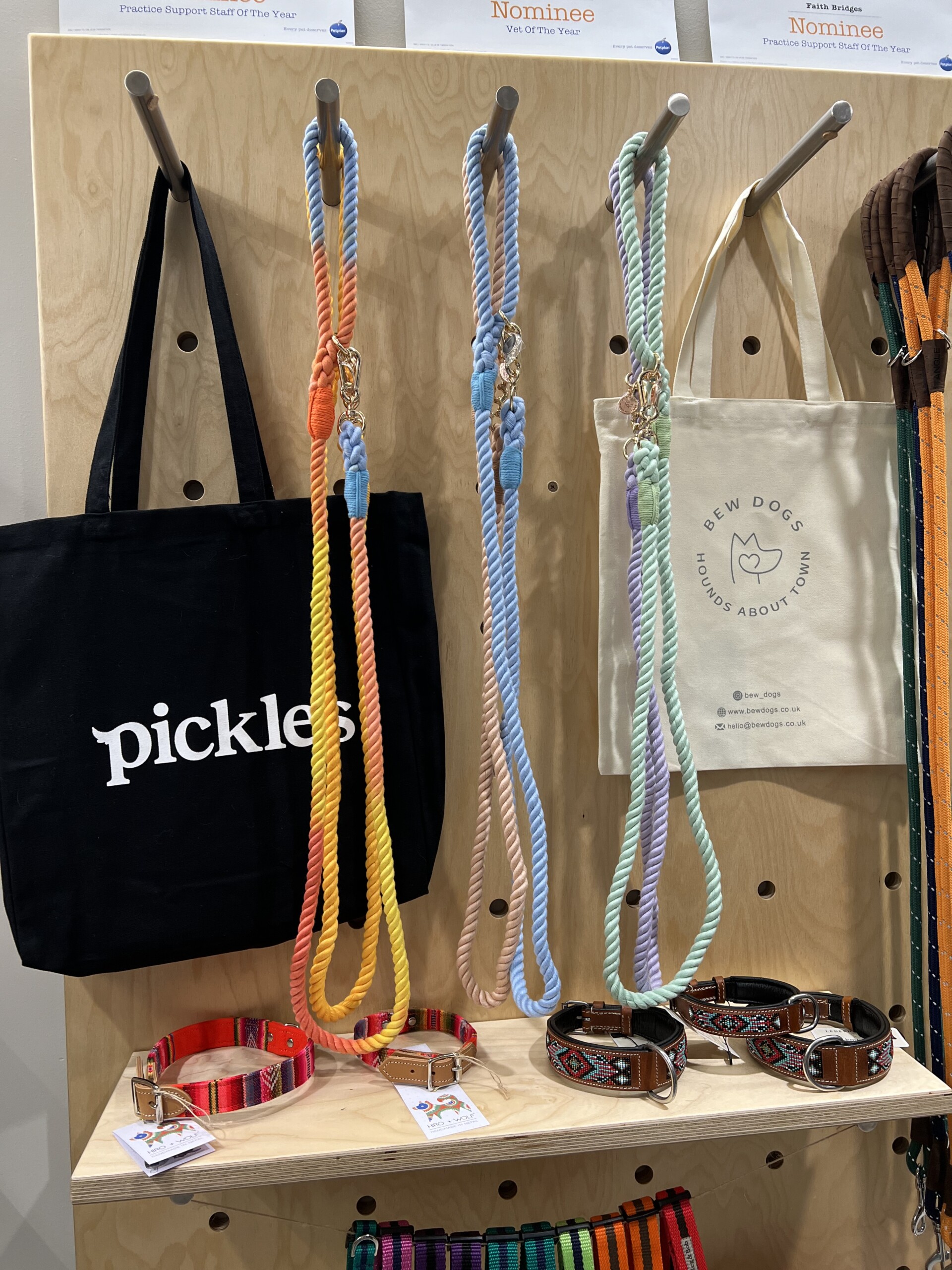 a wooden peg board against a wall in a vets has two canvas bags hanging and a range of colourful pastel rope leads for dogs and some collars on display too. 