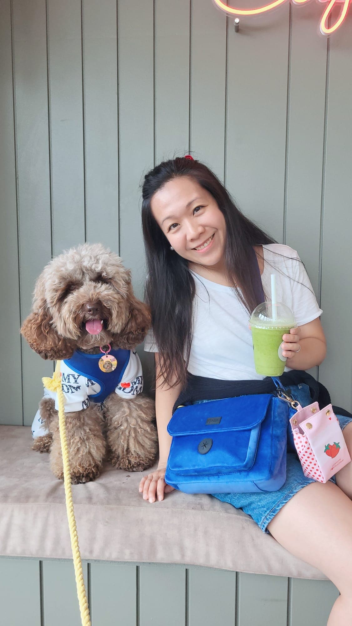 Girl with dog holding a green smoothie, sitting against a green wall.